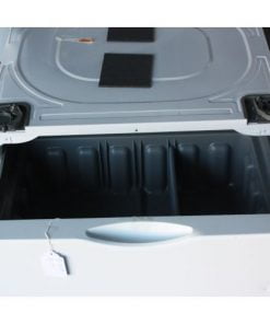 Open drawer of a large white appliance, likely a washing machine pedestal. The interior of the drawer is empty and divided into sections. Black padding material is visible on the top surface. A small plastic packet is also present on the top.